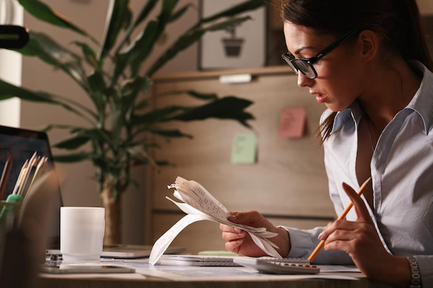 A female calculating tax bills while working at her desk in an office setting.