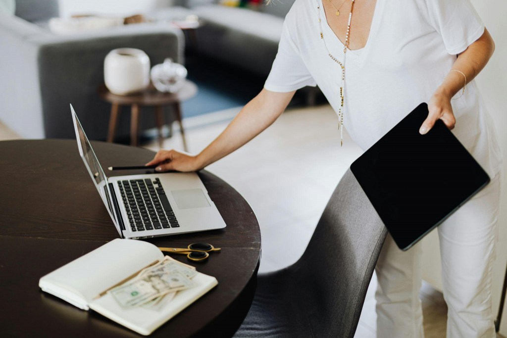 A woman stands at a table while working on her laptop.