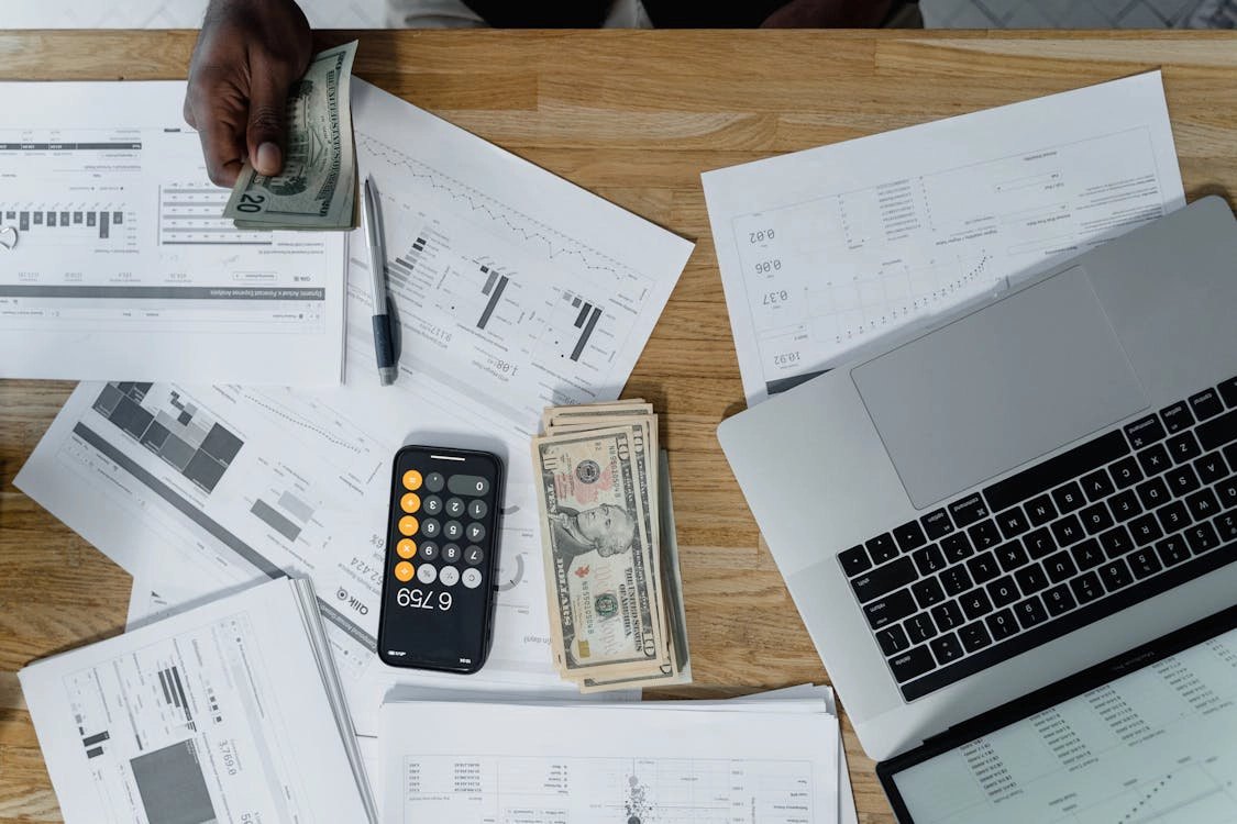 dollar bills, financial documents and an iPhone on a wooden surface